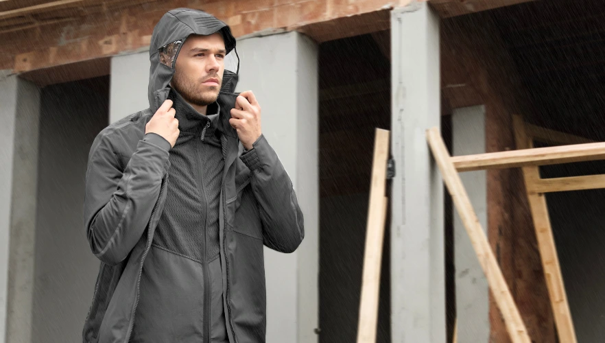 Eine Person trägt eine dunkle wetterfeste Jacke und zieht die Kapuze über den Kopf.