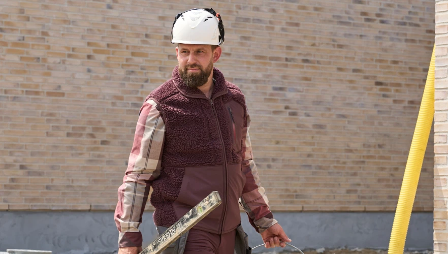 Eine Person trägt eine karierte Arbeitsjacke und hält ein langes Messwerkzeug in der Hand.